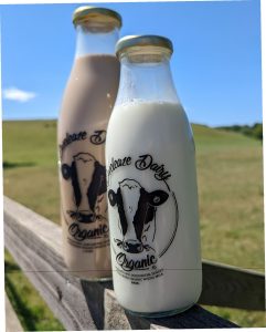 Two bottles of Eweleaze Dairy organic milk against Dorset countryside landscape