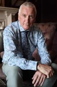 "Portrait of Jim Johnson, photographer of Dorset churches interior project, seated wearing blue patterned shirt and tie"