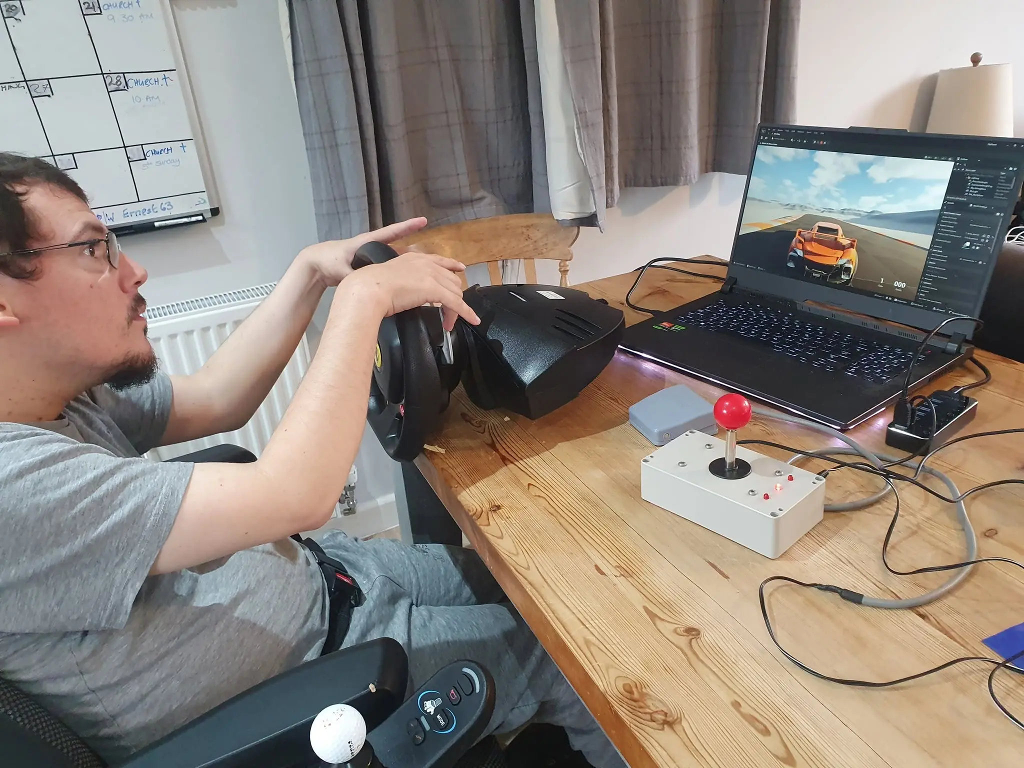 Louis Gale, founder of the Accessible Gaming Café in Dorchester, using an adapted steering wheel and joystick controller to play a racing game on his laptop.