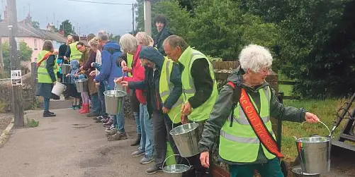 "Villagers in high-vis vests form a bucket chain during a re-enactment demonstrating historic firefighting methods, held to campaign against Dorset and Wiltshire Fire and Rescue station closures