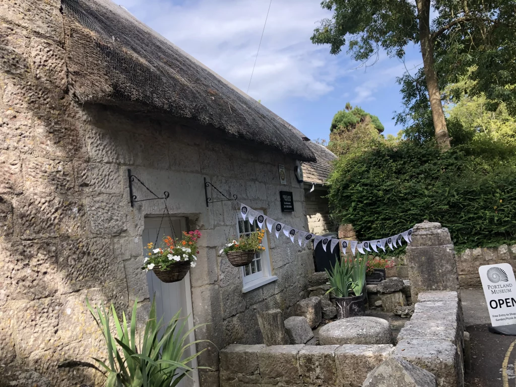 Portland Museum's thatched stone building with hanging flower baskets and open sign during the archaeology festival