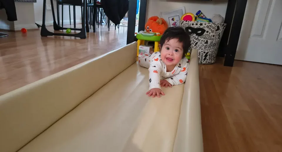 Baby Daniel, who has Down's Syndrome, crawling along tracks built as part of REMAP's disabled adaptations to help disabled children with mobility at home