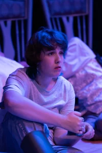 Women of Dorset performer sits in a moment of quiet reflection on stage, lit in blue and purple tones