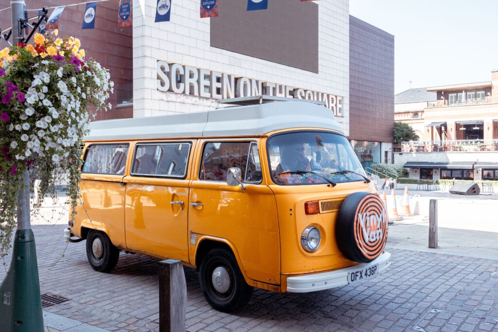 Vintage orange VW campervan branded "Vinyl Van" parked outside the Screen on the Square cinema at Brewery Square.