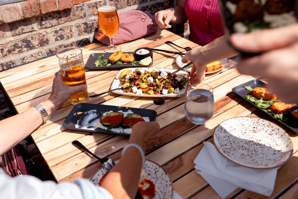 Sharing plates of Turkish meze, salad and grilled aubergine on an outdoor table at Meram Kitchen, Brewery Square.