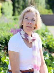 Catherine Maddocks, 76, who runs Concerts in the West, working past retirement age, sits in a sunny garden wearing a pink striped scarf.