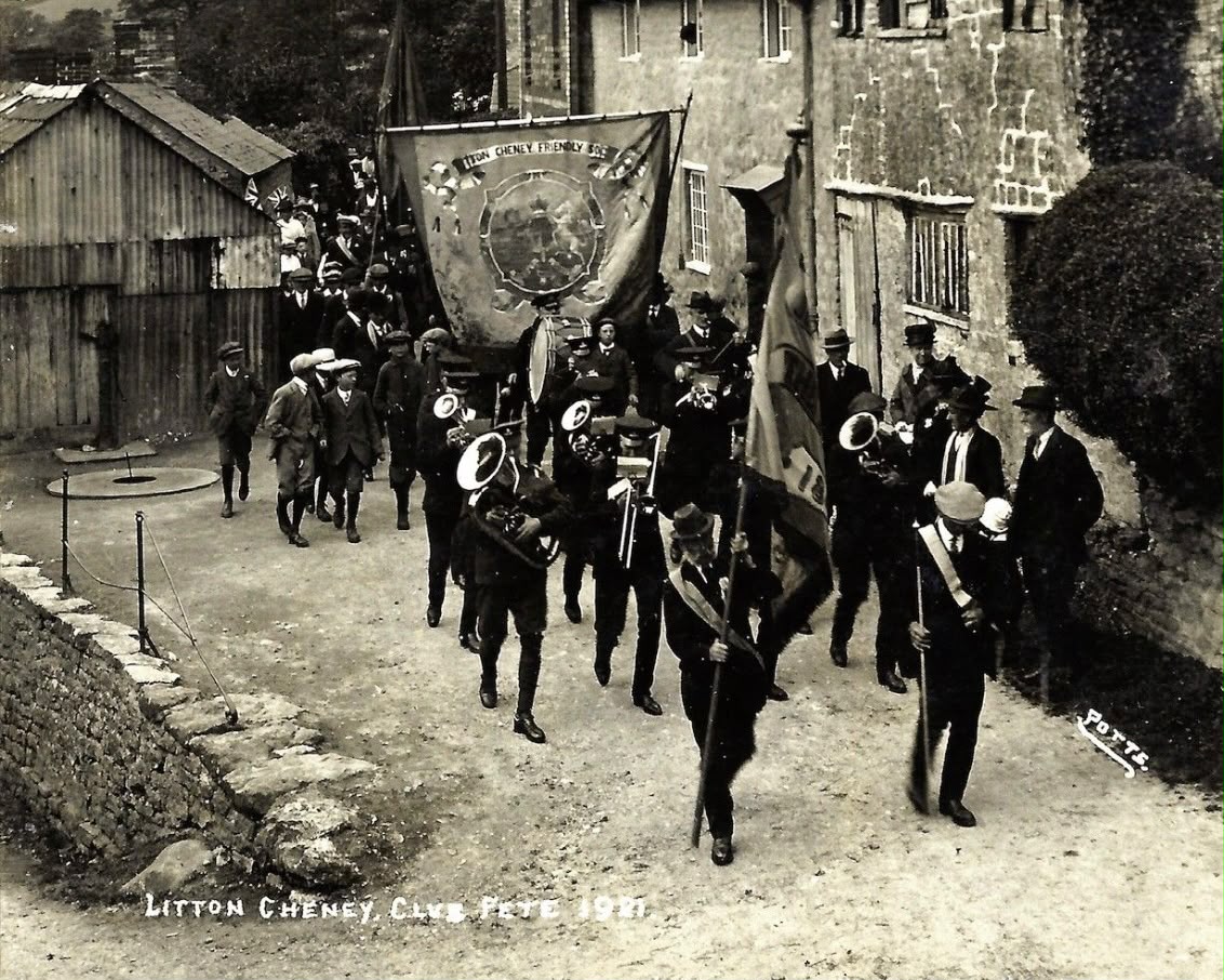 Litton Cheney Friendly Society Club Day Parade, 1921: a brass band marches past stone cottages behind the society's banner.