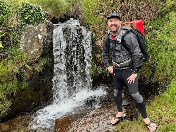 Weymouth man carries postbox 650 miles for Head Outside charity: Stu Skinner MBE smiles beside a waterfall with the red postbox strapped to his backpack