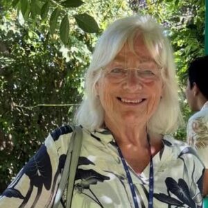 Lindsey Howell, 79, organiser of Bryanston and Canford fairs, working past retirement age, smiles outdoors wearing a lanyard and floral shirt.